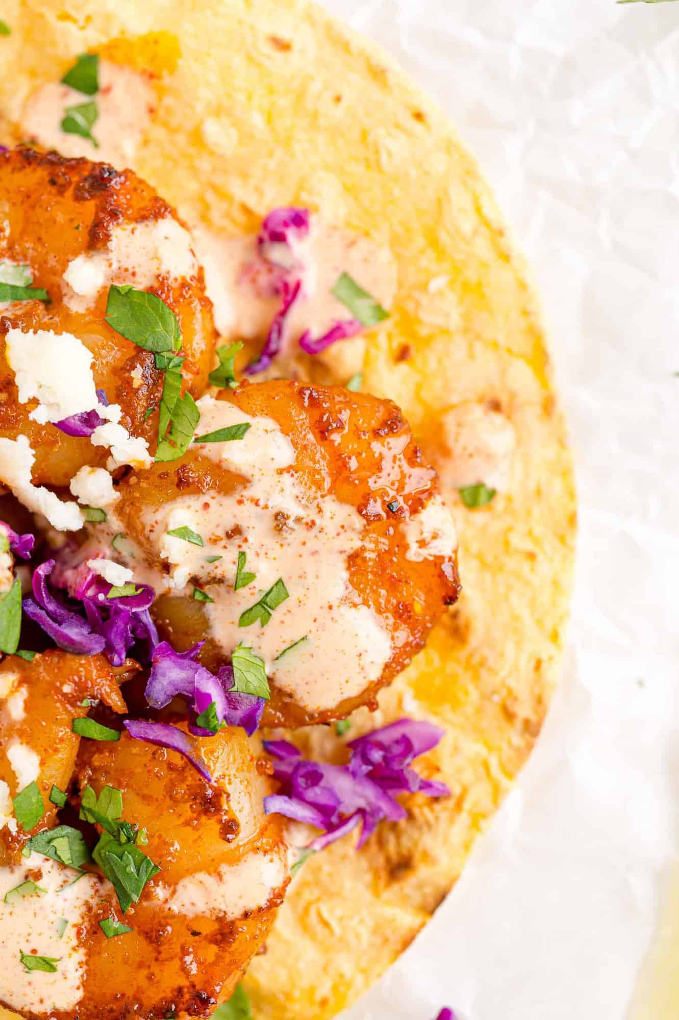 Close up view of shrimp and sauce on corn tortilla.