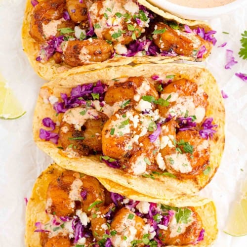 Three shrimp tacos with creamy drizzle and cotija cheese.