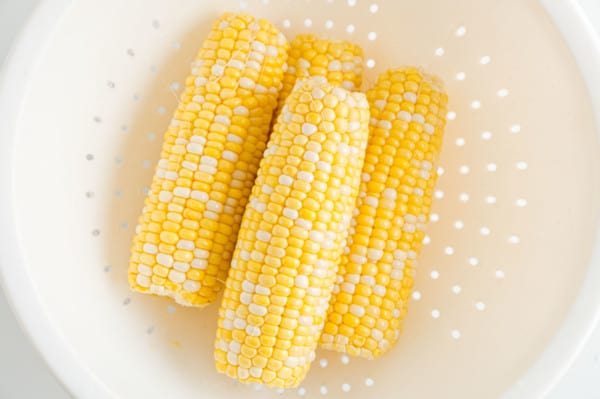 Overhead view of four ears of corn in a white collander.