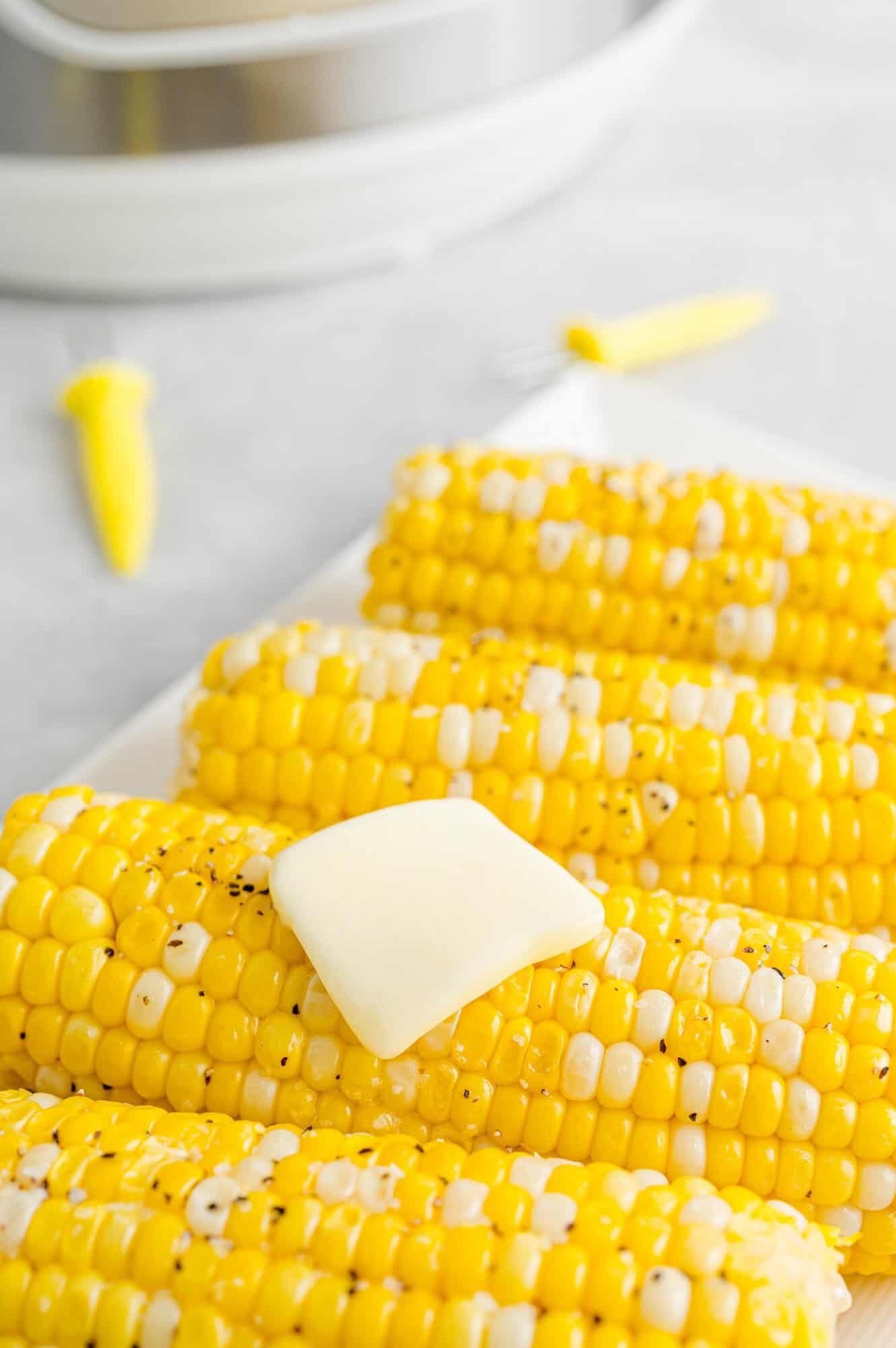 Four ears of Instant Pot corn on the cob topped with butter, salt, and pepper served on a white rectangular platter.
