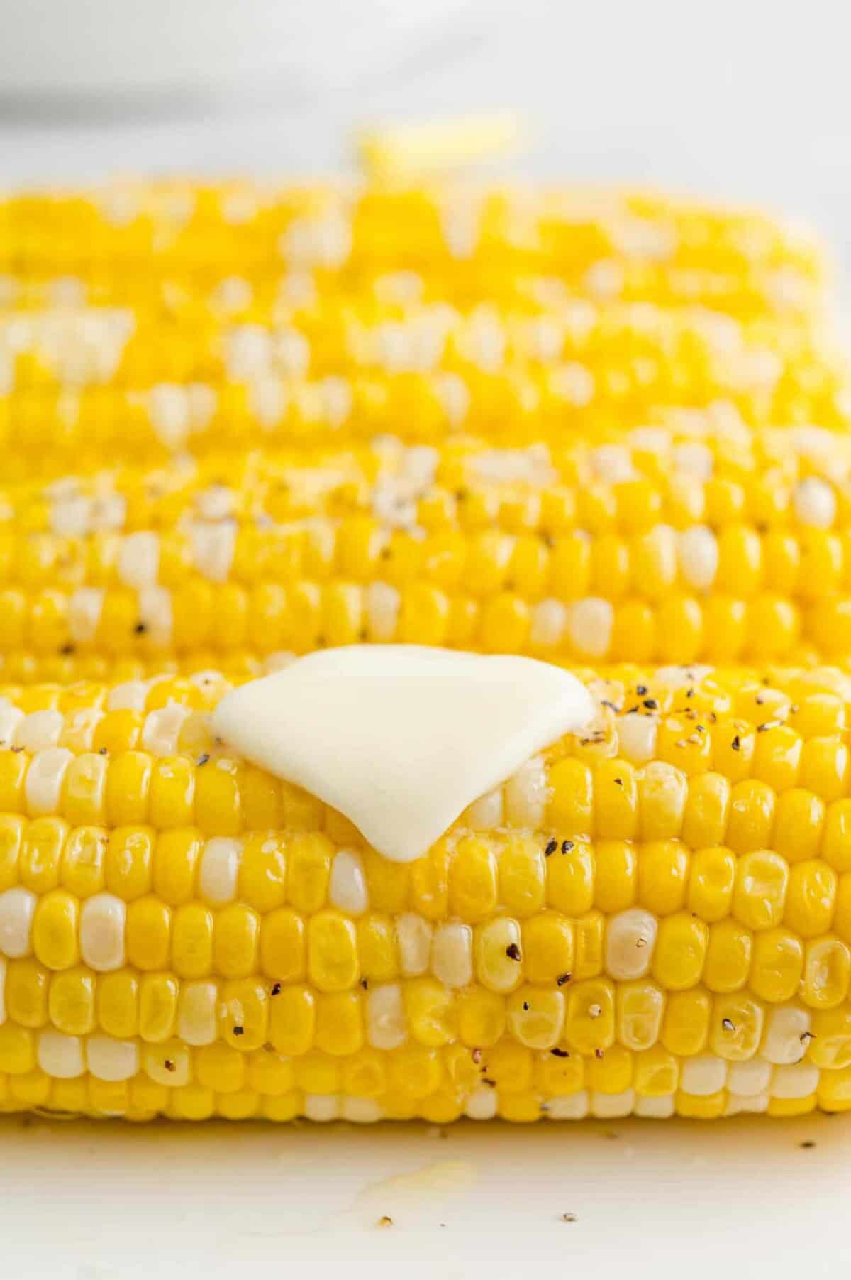 Close up of Instant Pot corn on the cob topped with a pat of butter, salt, and pepper, with more corn in the background.