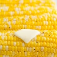 Close up of Instant Pot corn on the cob topped with a pat of butter, salt, and pepper, with more corn in the background.