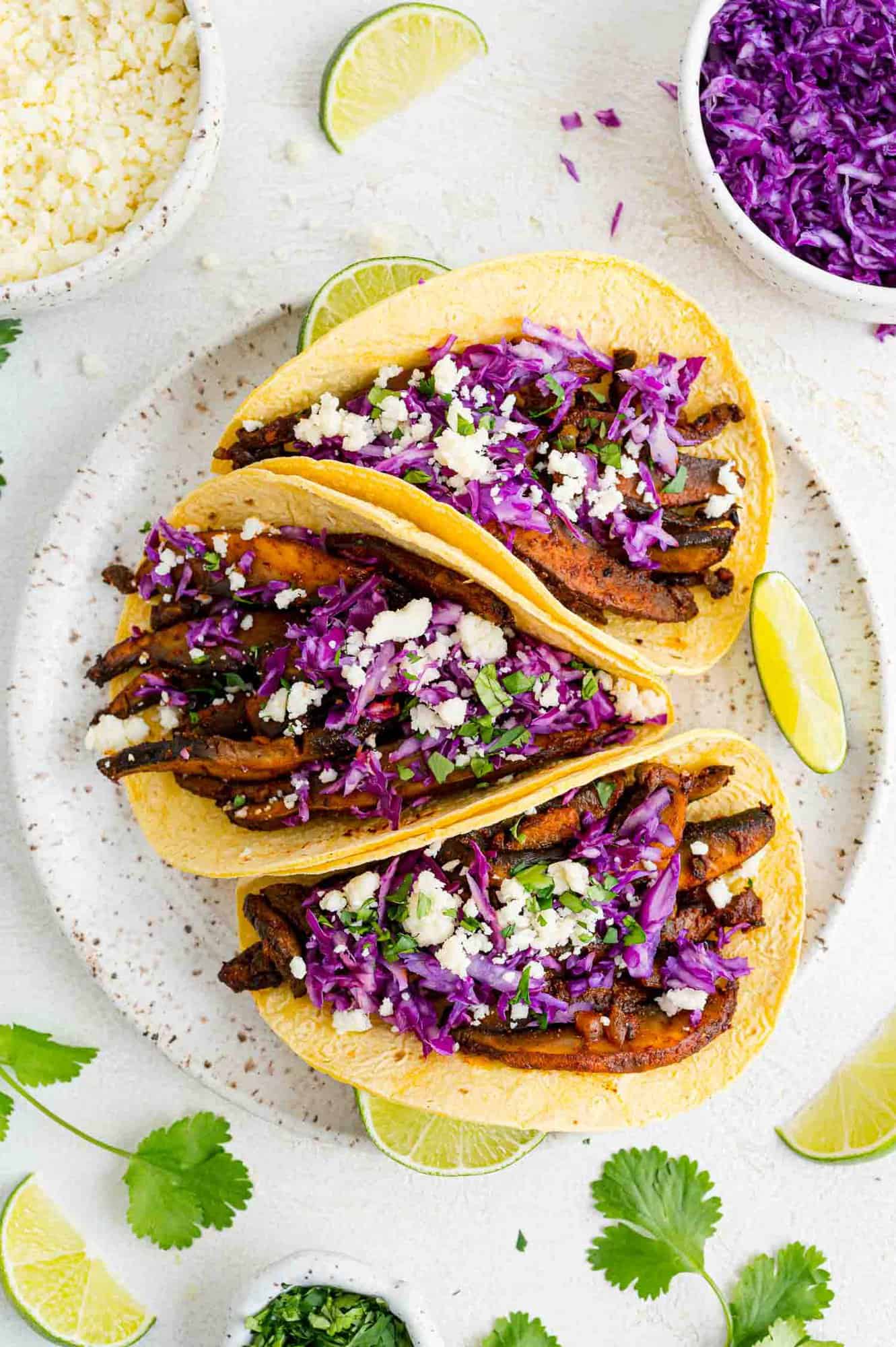 Three tacos on a platter with toppings nearby.