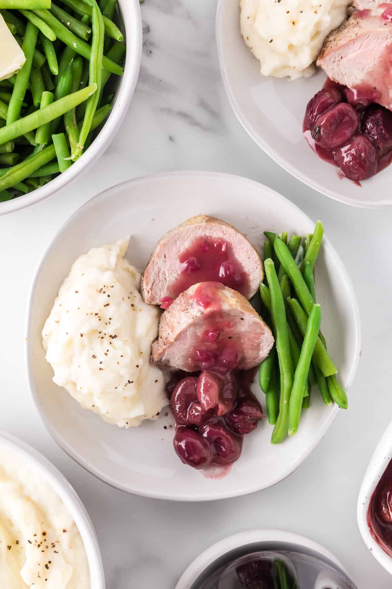 Plated pork tenderloin with sauce, green beans, mashed potatoes.