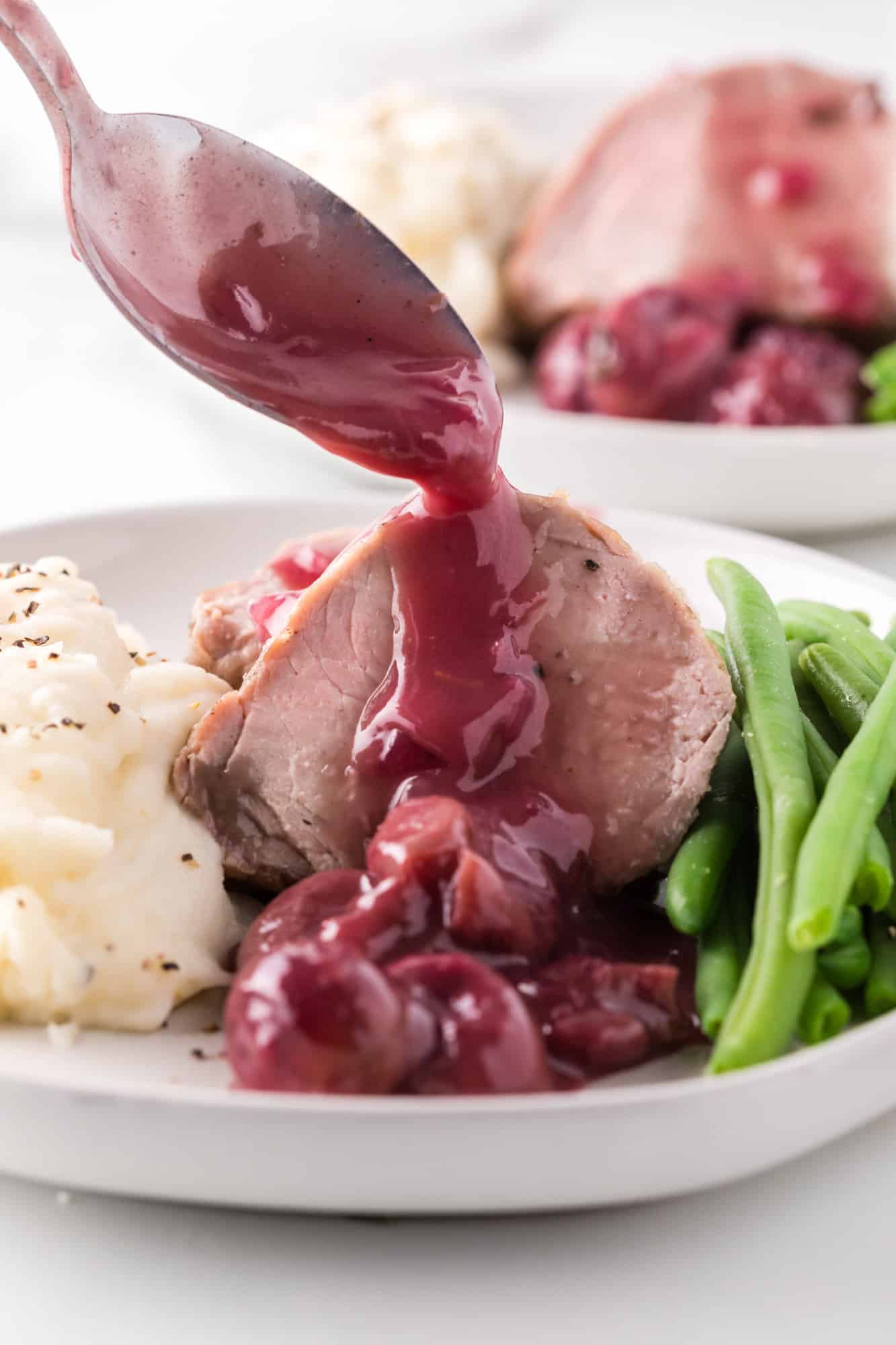 Pork tenderloin with port wine sauce being added to top of slices.