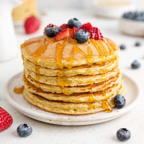 Quinoa pancakes stacked with berries and syrup.