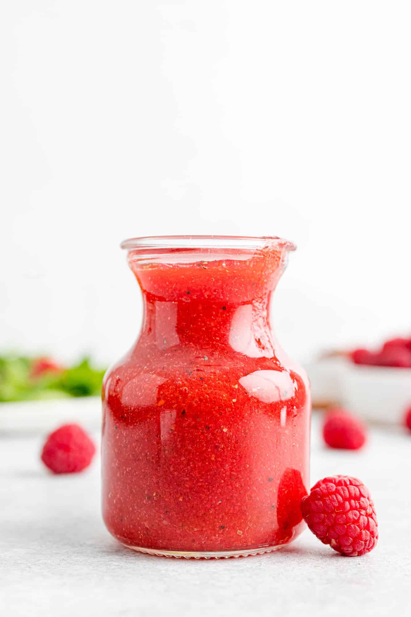 Fresh raspberry vinaigrette in a small container with fresh raspberries nearby.