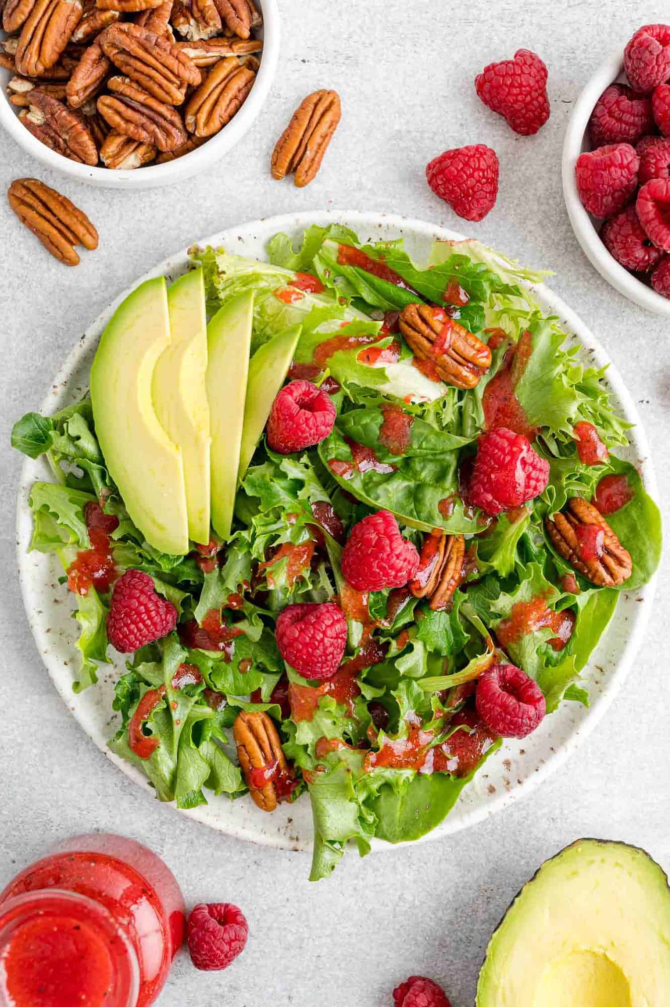 Dressing on a salad with raspberries, pecans, avocado.