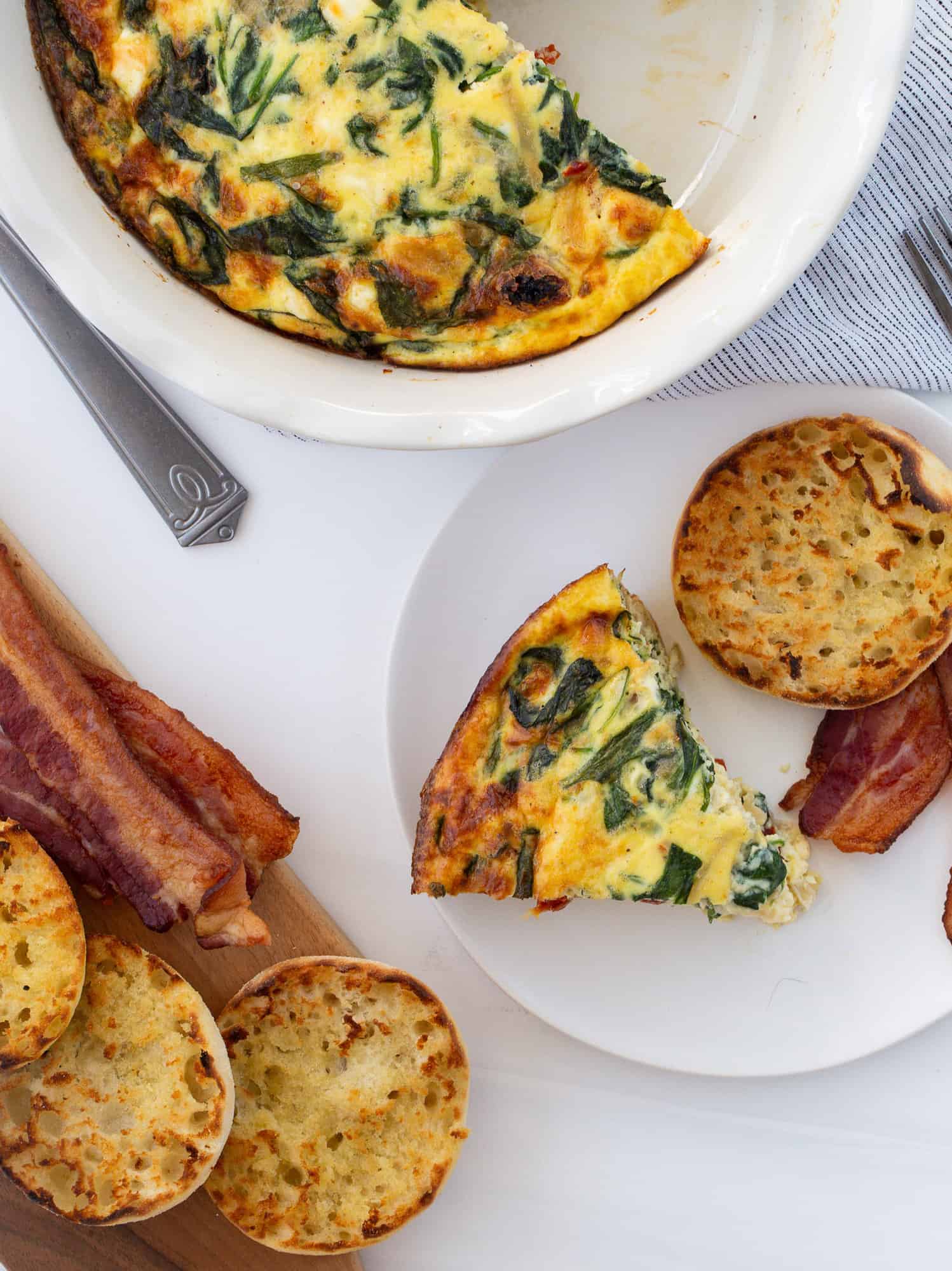 Overhead view of quiche with a slice out of it, served with english muffin.