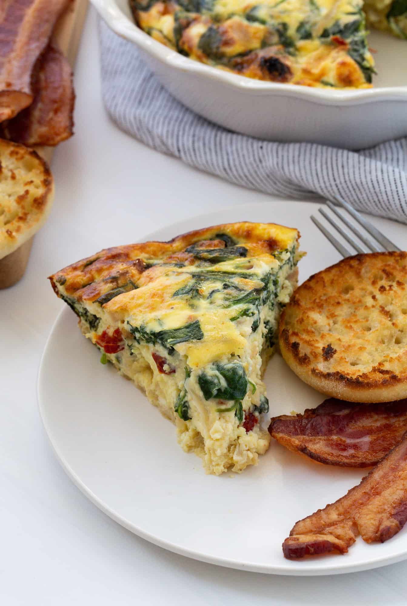 Crustless quiche on a plate with an english muffin and bacon.