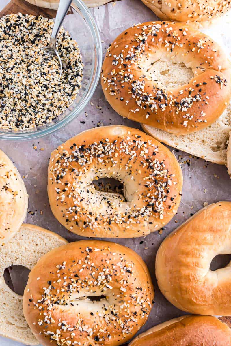 Overhead view of assorted everything bagels next to a bowl of everything bagel seasoning.
