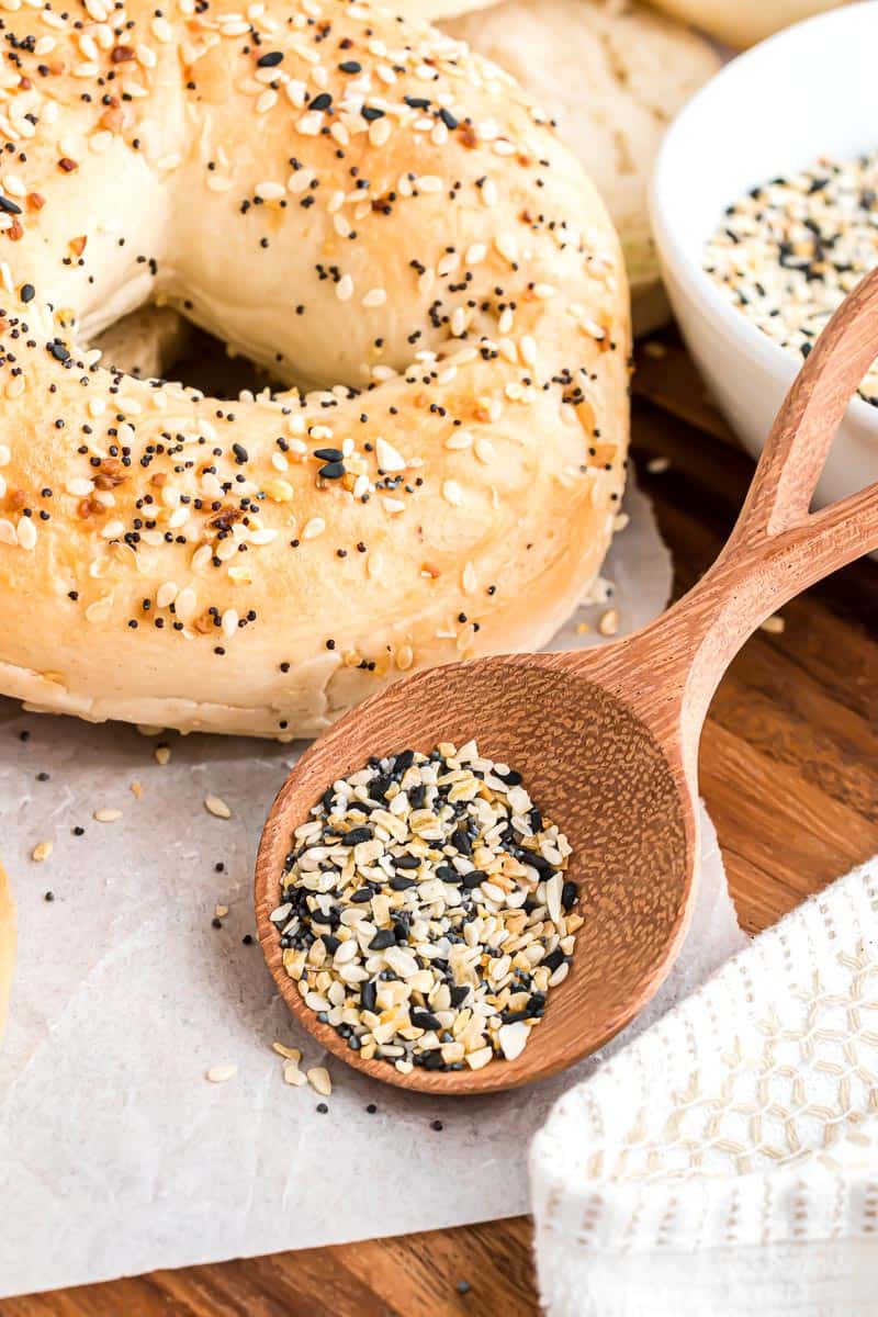 Make homemade everything bagel seasoning in minutes with only 5 ingredients. Perfect for seasoning bagels, veggies, and just about everything! A wooden spoonful of everything bagel seasoning leaning against a bowl next to an everything bagel.