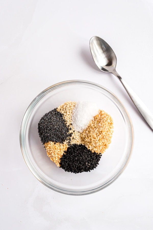 Everything bagel seasoning ingredients combined in a mixing bowl next to a spoon.