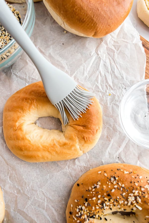 A rubber basting brush coats a plain bagel with water, to be coated with everything bagel seasoning.