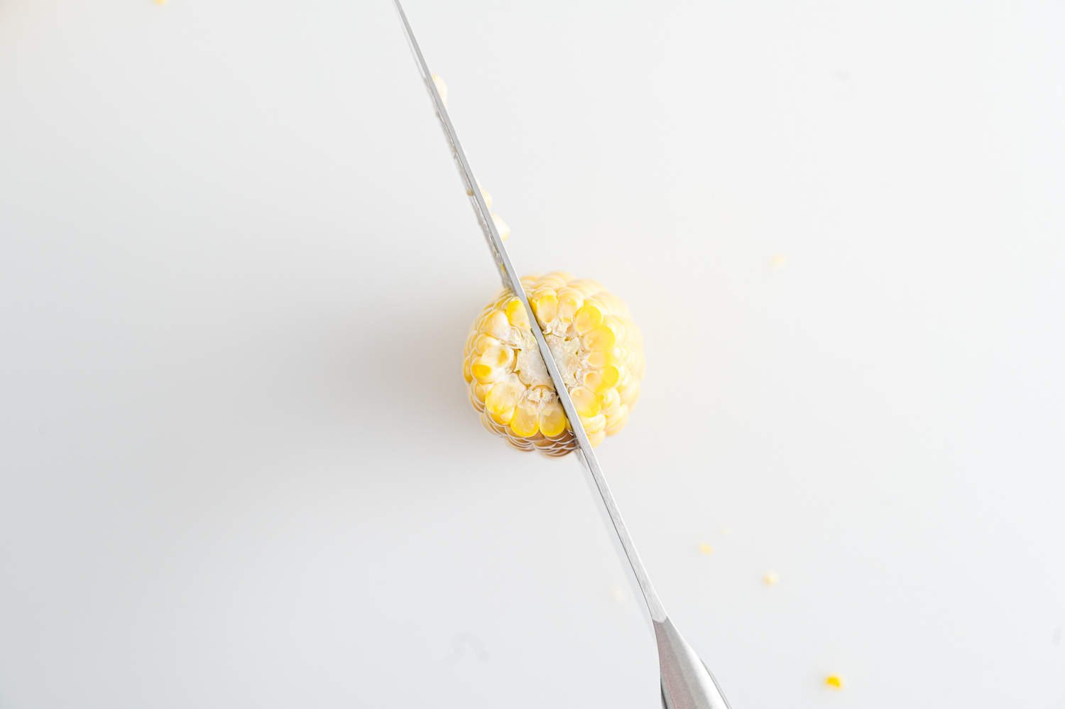 Ear of corn being cut in half lengthwise.