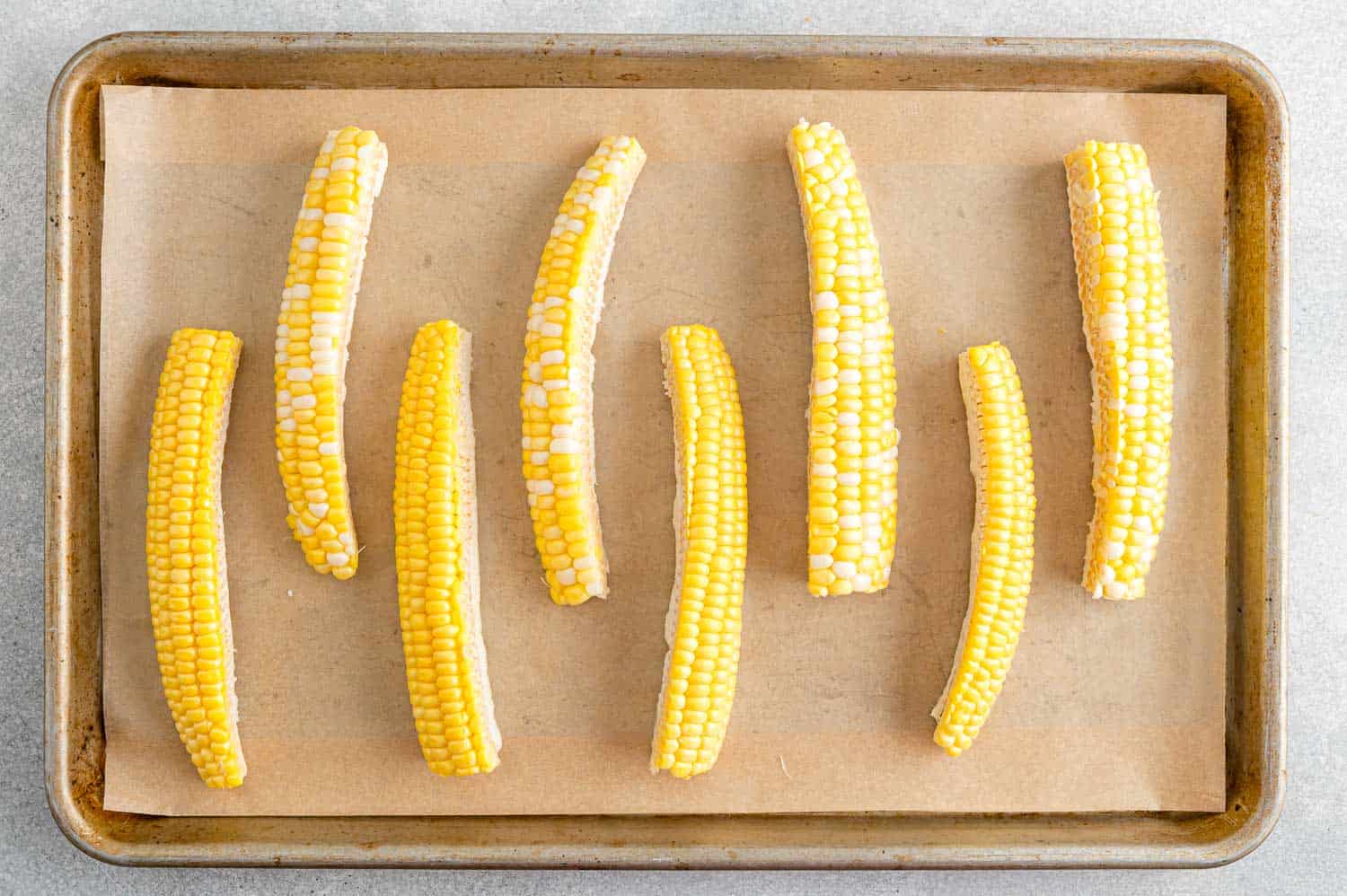 Unseasoned, uncooked corn ribs on a parchment paper lined sheet pan.