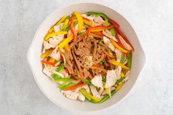Garlic and jerk seasoning added to a skillet with chicken and sauteed bell peppers.