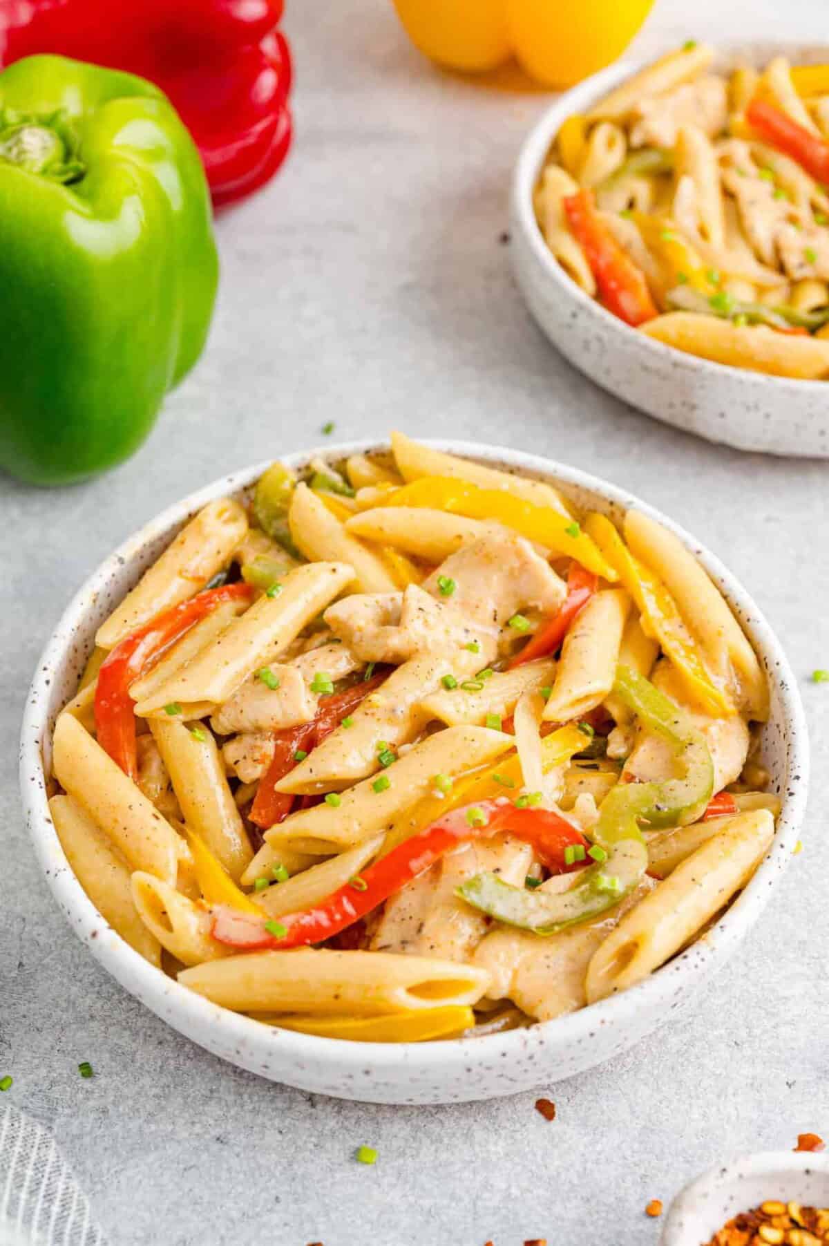 Bowls of Rasta Pasta next to red, green, and yellow bell peppers on a countertop.