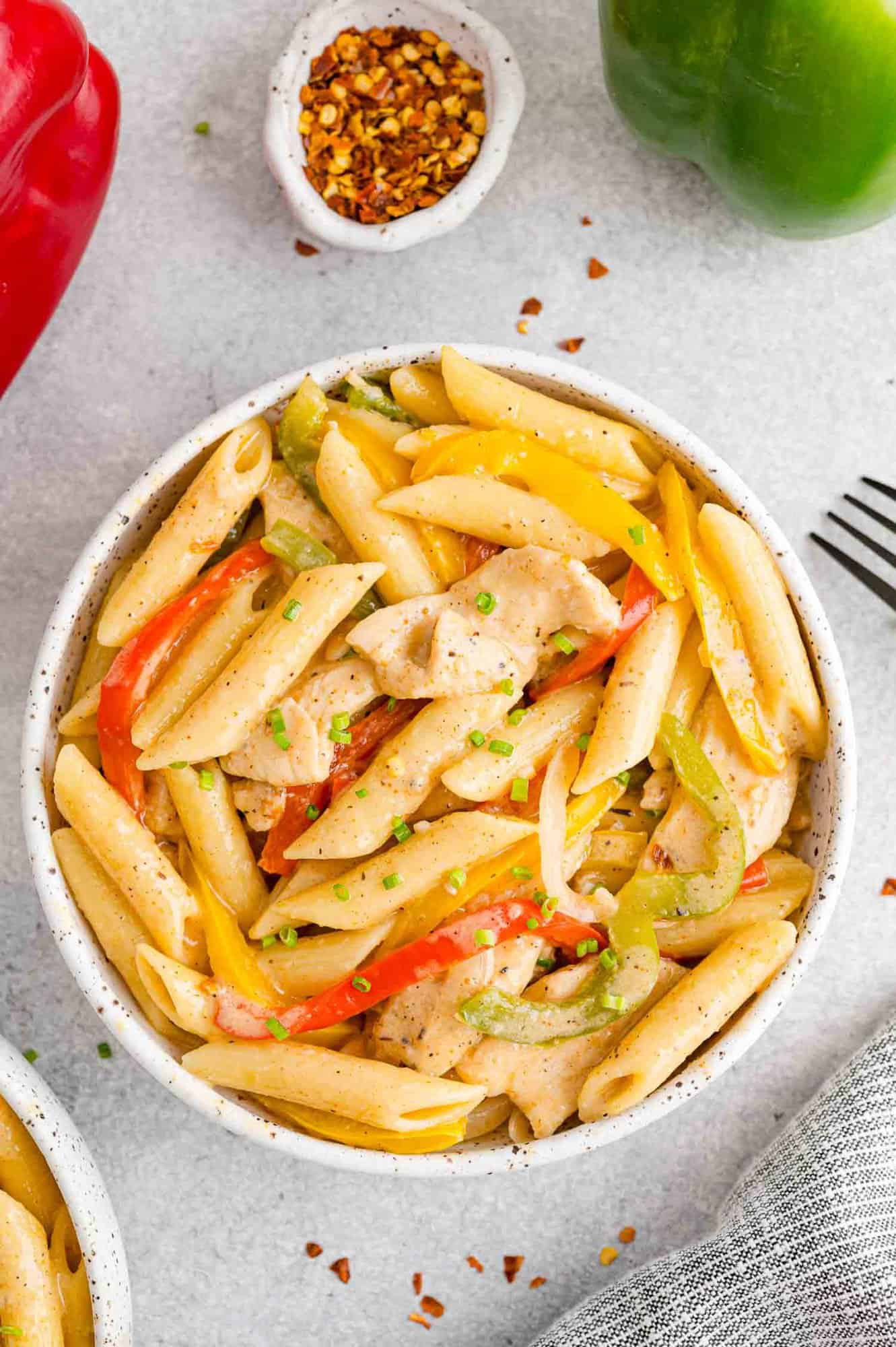 Overhead view of a bowl of Rasta Pasta next to a smaller bowl of crushed red peppers.