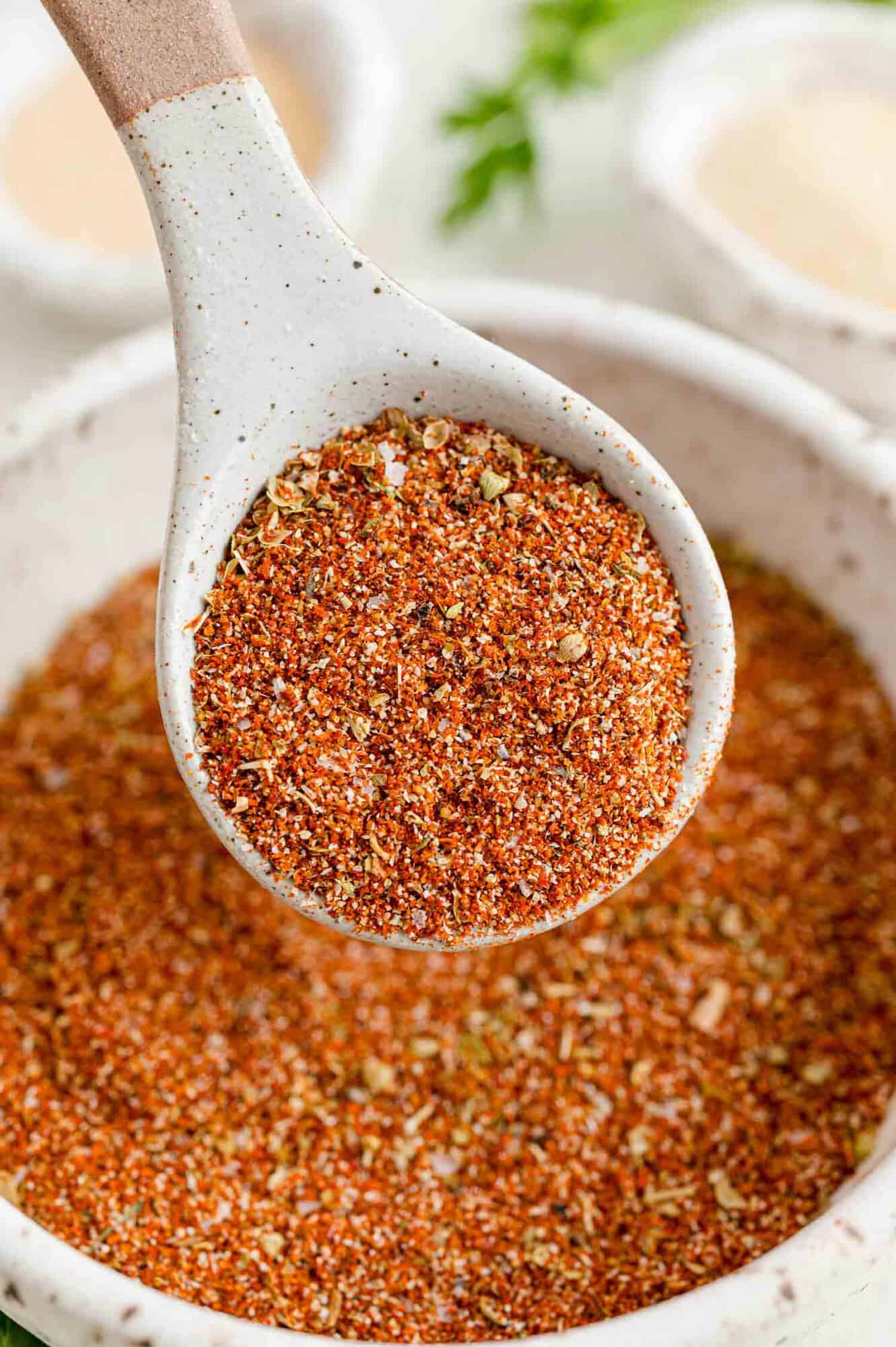 A spoonful of Southwest spice blend held over a bowl of seasoning.