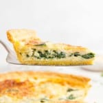 Spinach quiche on a pie server, held above the rest of the quiche.