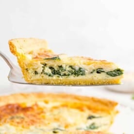 Spinach quiche on a pie server, held above the rest of the quiche.