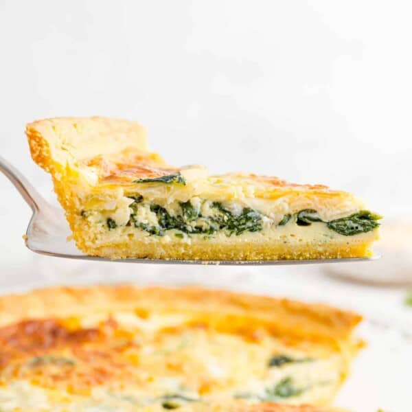 Spinach quiche on a pie server, held above the rest of the quiche.