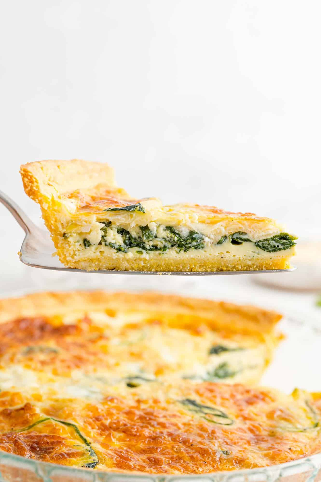 Spinach-Quiche-with-cornmeal-crust Quiche being served using a pie server, remaining quiche in background.