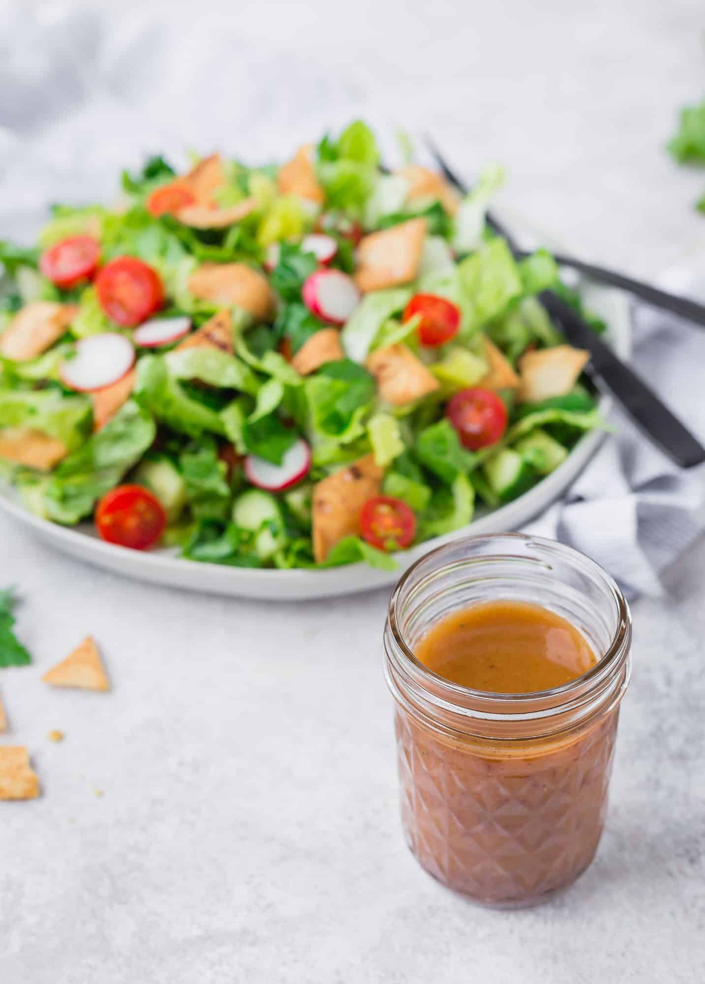 Fattoush salad with dressing in a jar in foreground of photo.