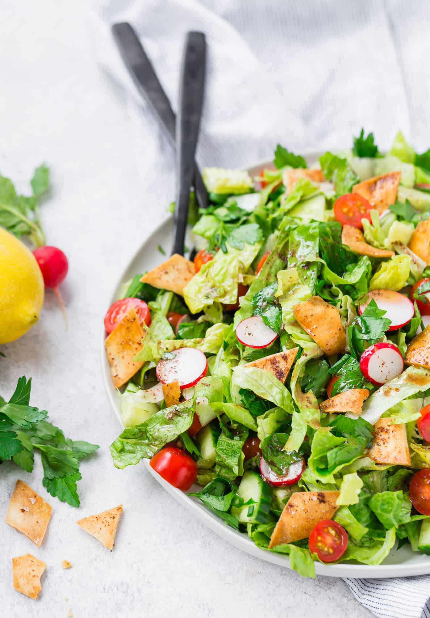 Fattoush salad on a large serving platter with black utensils.