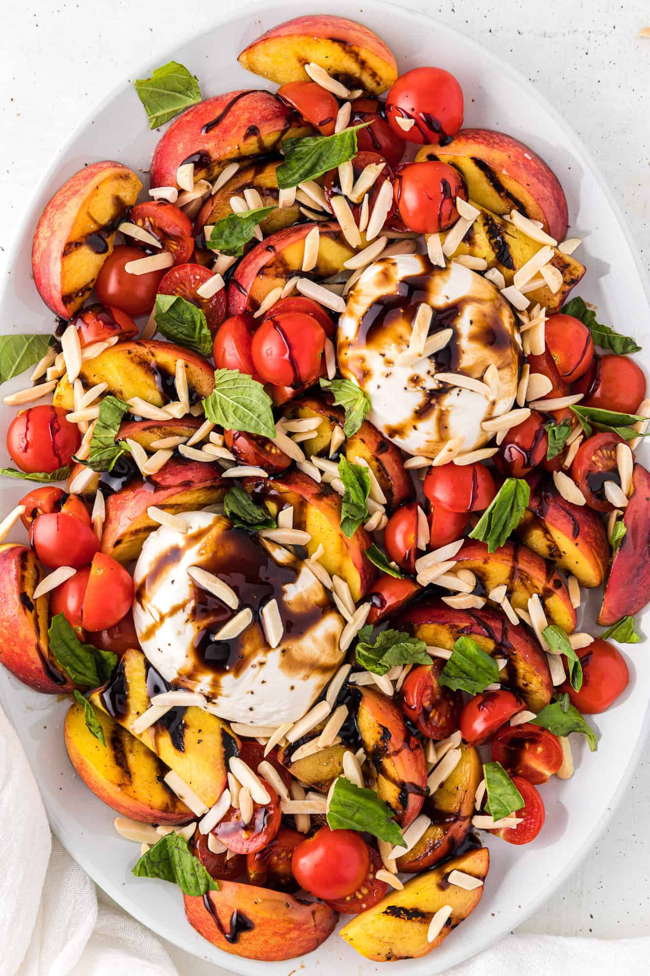 Grilled peach salad arranged around burrata cheese, topped with almonds.