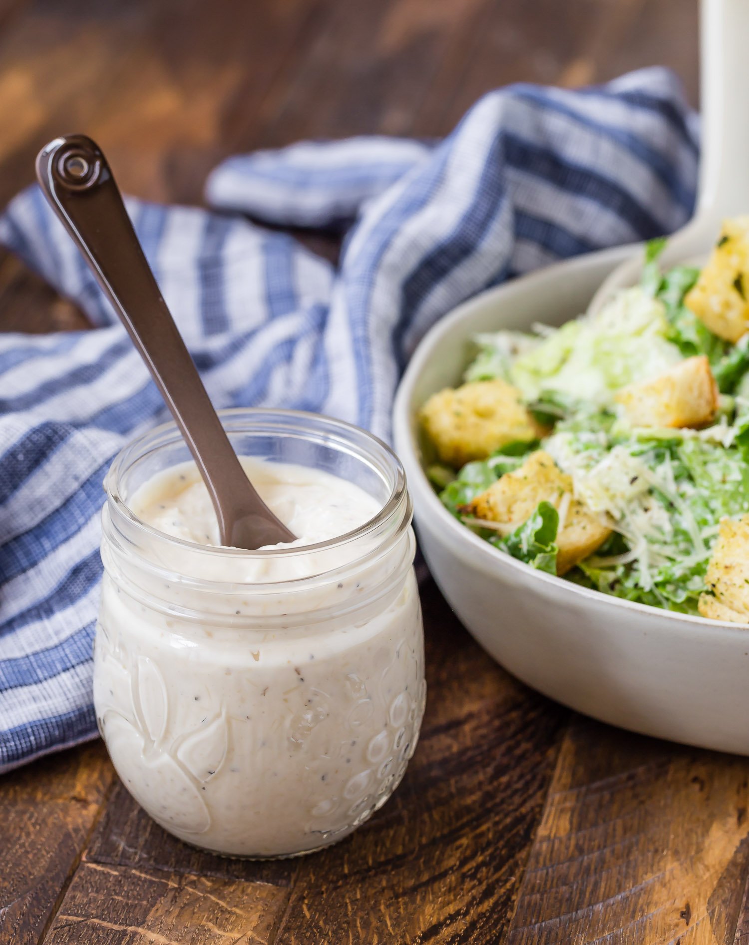 Homemade caesar salad dressing in a jar, salad in background.