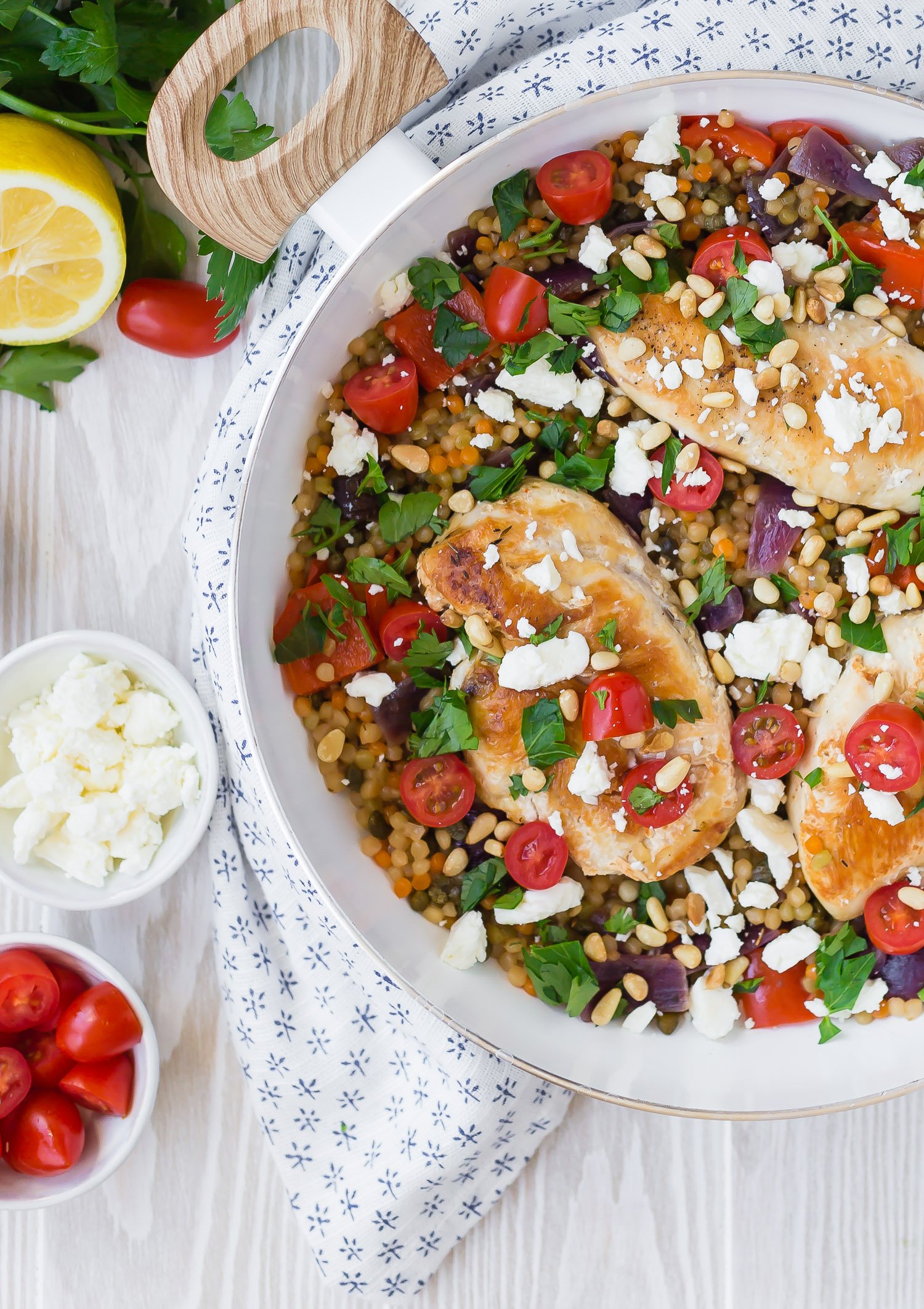 One pan chicken and couscous in a white frying pan, topped with tomatoes and parsley.