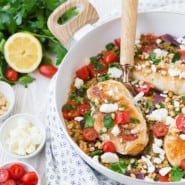 Chicken and couscous in a white frying pan with a wooden spoon.