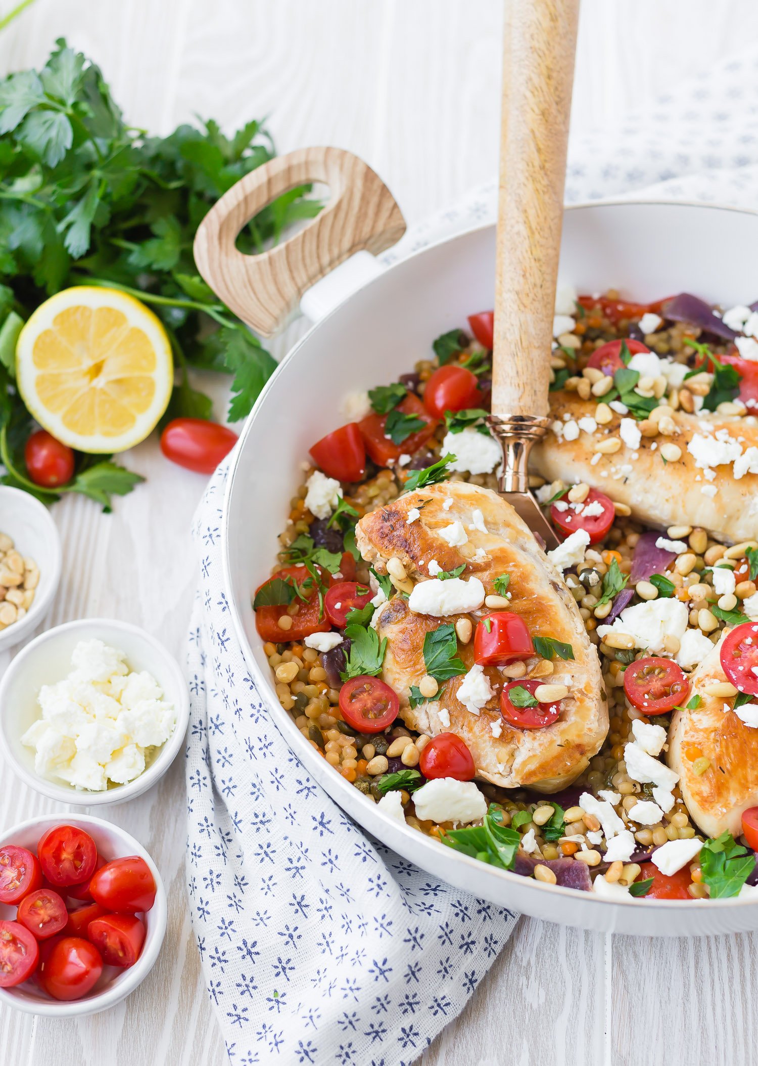 Chicken and couscous in a white frying pan with a wooden spoon.