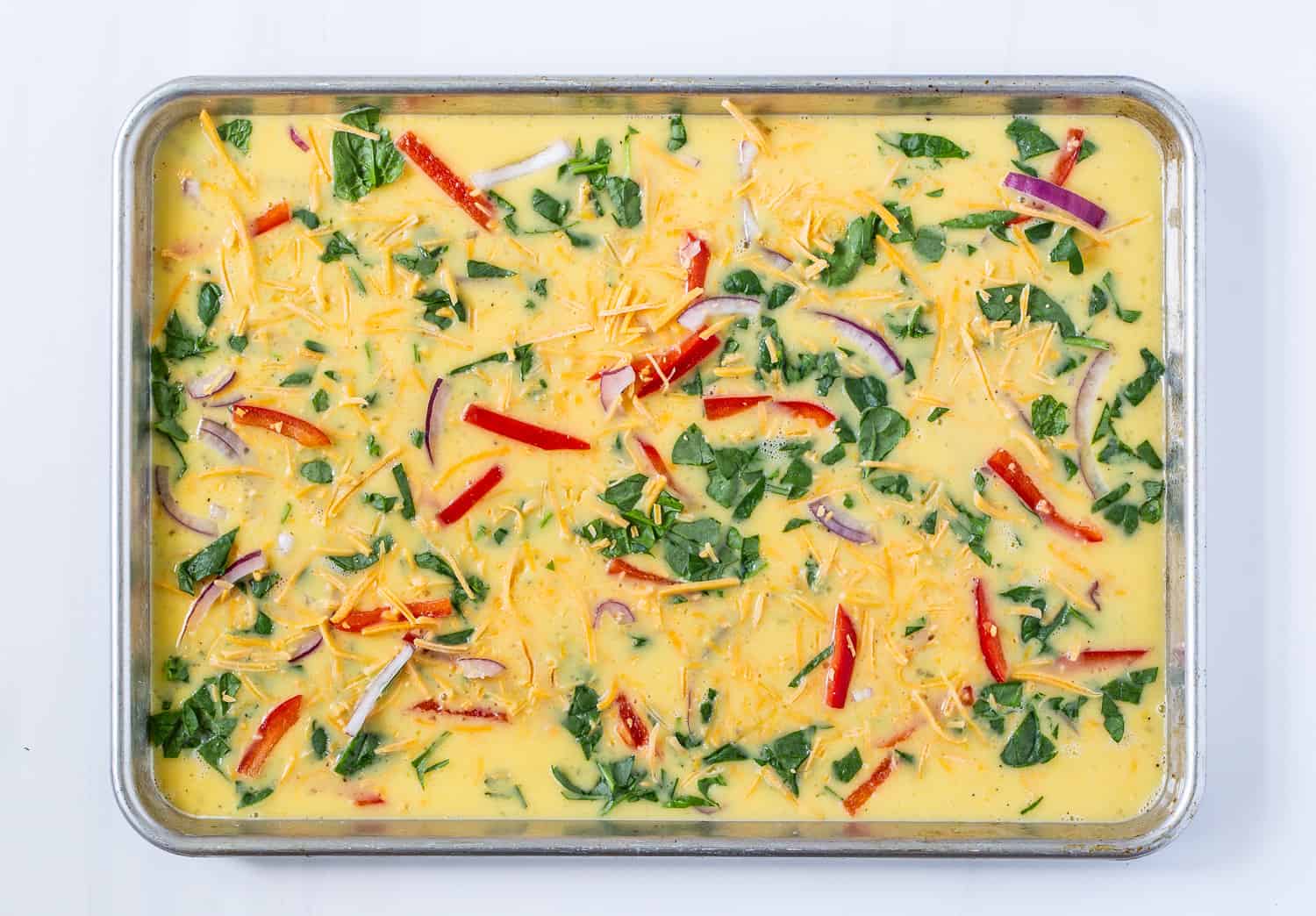 Sheet pan eggs, unbaked, toppings added.