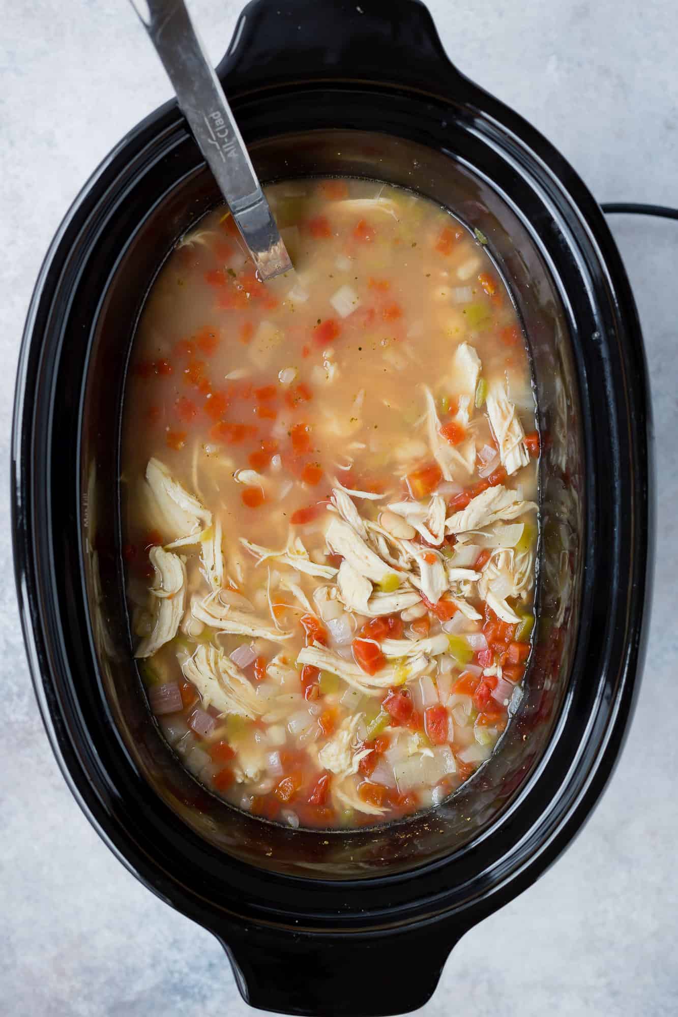 White chicken chili in a slow cooker with a ladle,