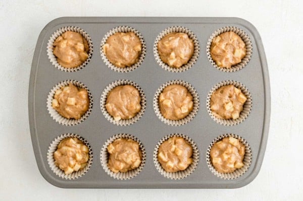 Apple muffin batter in a muffin tin, not yet baked.