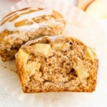 A glazed apple cider muffin cut in half to reveal chunks of apples inside.