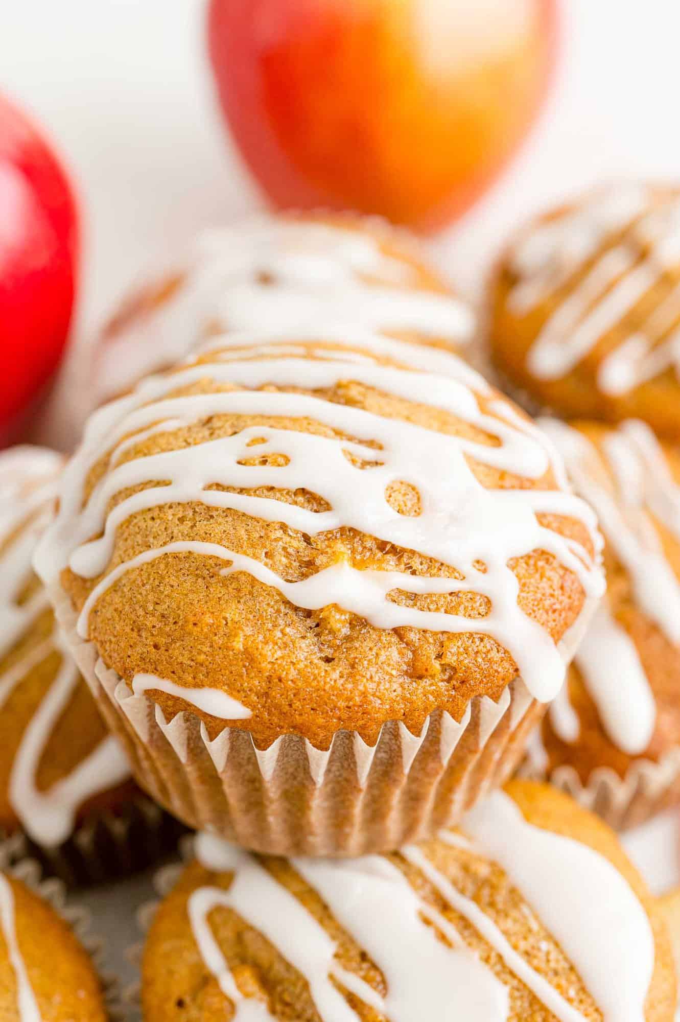 Close up of a stack of glazed apple cider muffins with apples in the background.