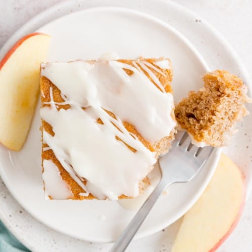 Overhead view of a slice of apple spice cake on a plate with a forkful missing.