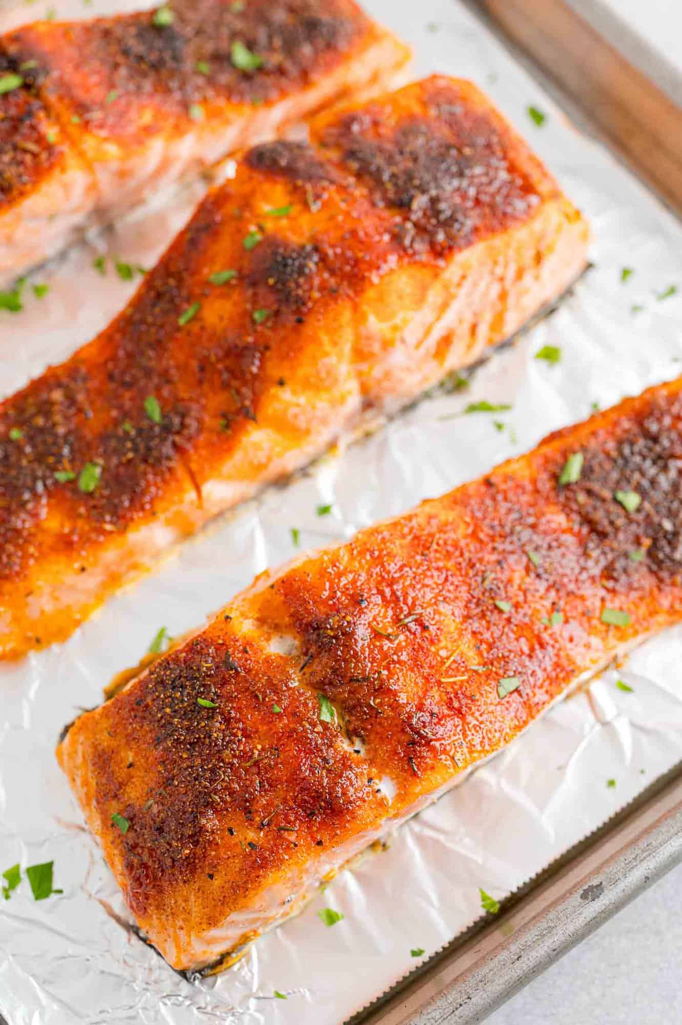 Close up of broiled salmon filets on a foil-lined baking sheet.