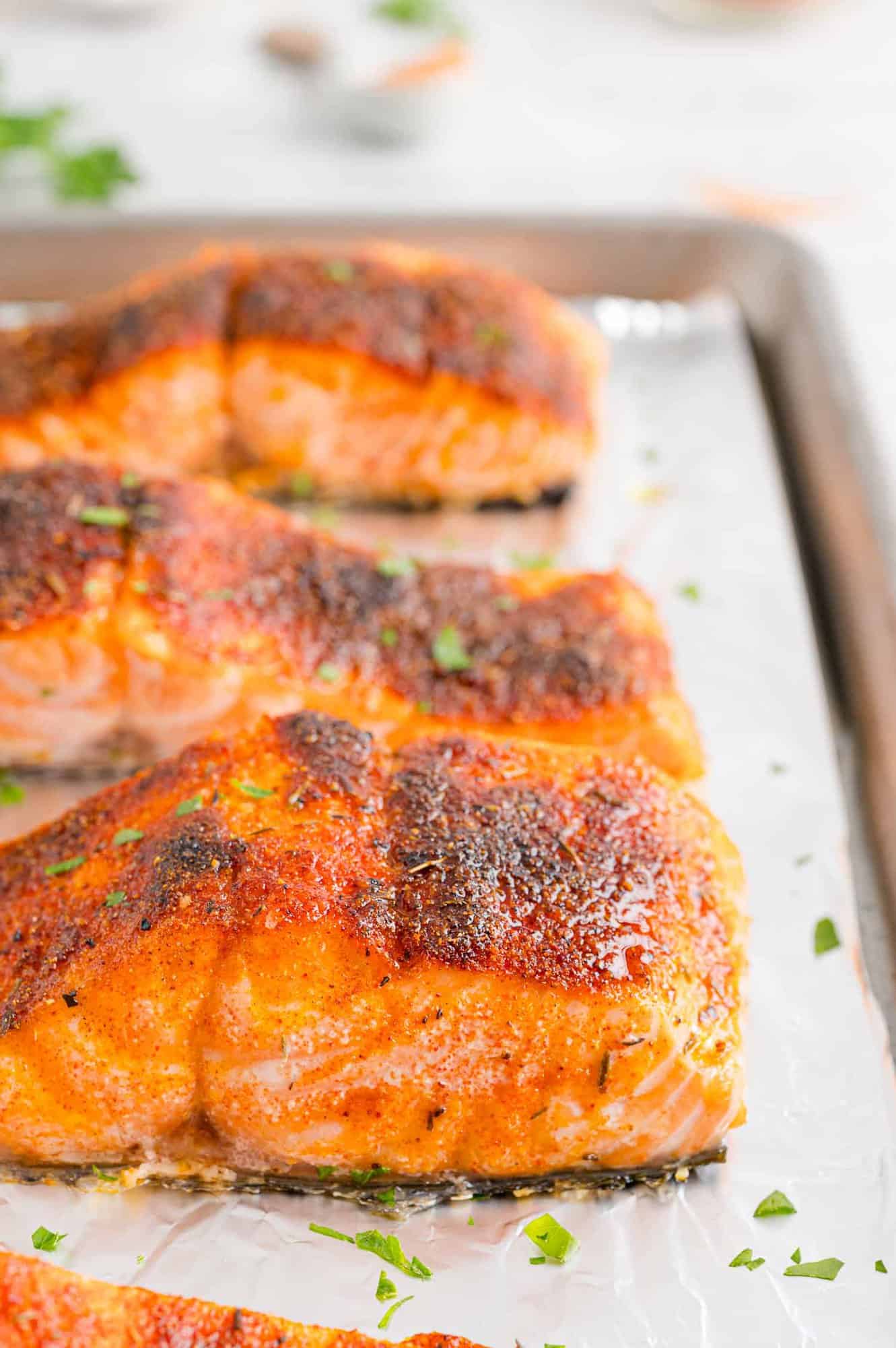 Close up side view of broiled salmon filets on a foil-lined baking sheet.