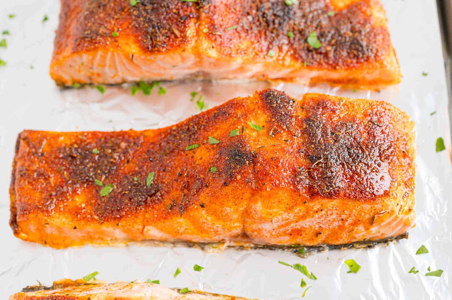 Close up of broiled salmon filets on a foil-lined baking sheet.