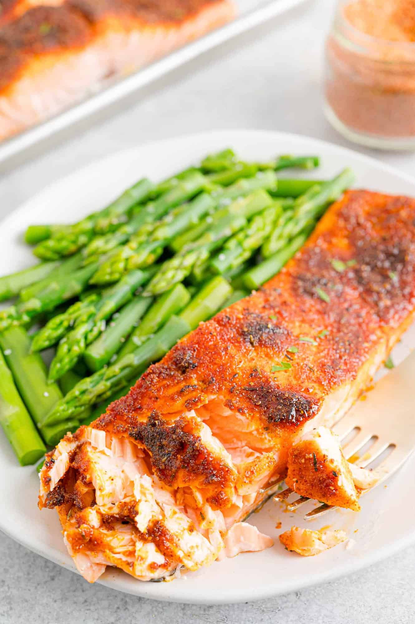 A broiled salmon filet with the corner partially flaked, next to a side of green beans on a white plate.