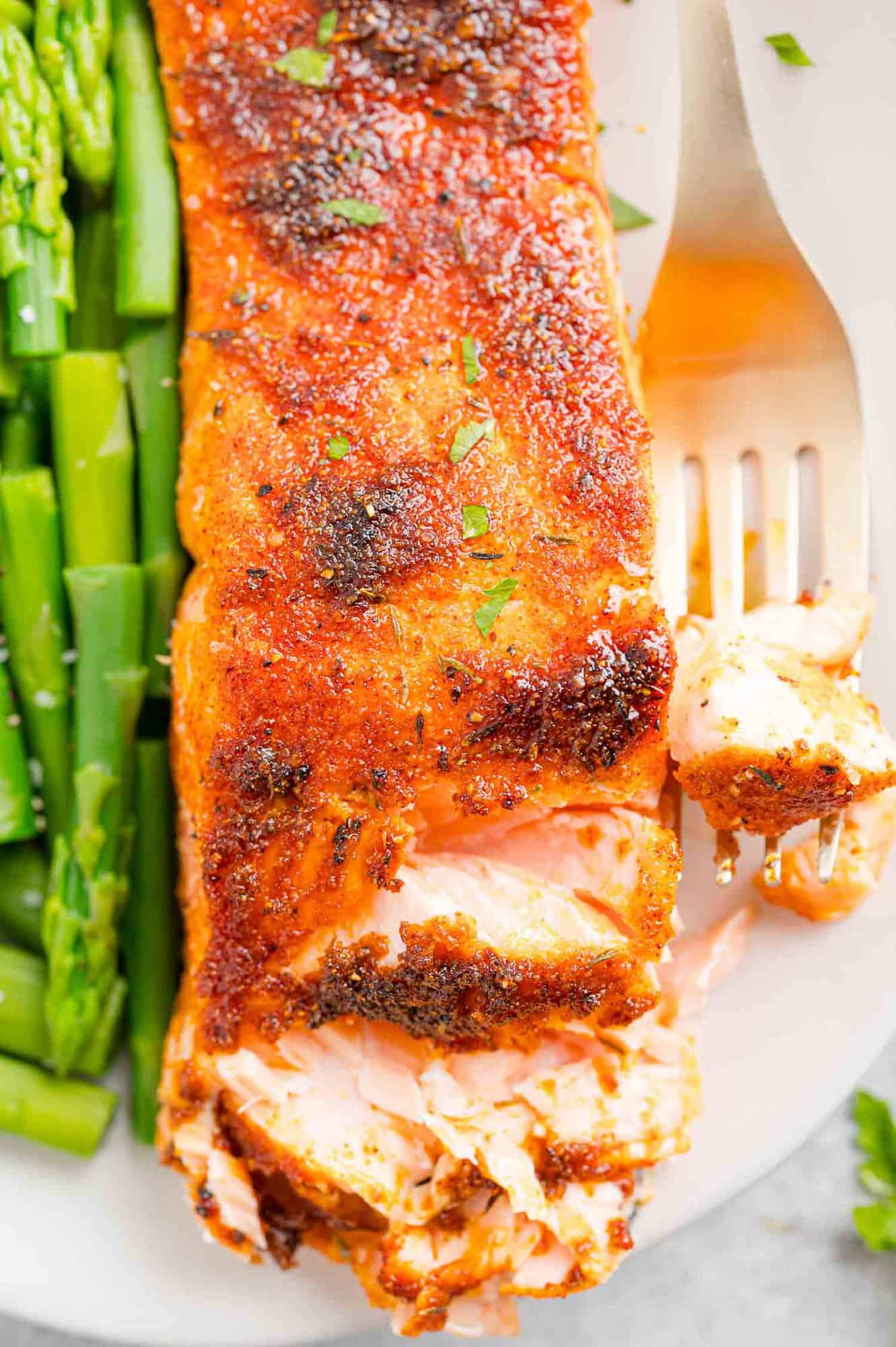 A forkful of salmon next to a flaked salmon filet on a plate with a side of green beans.