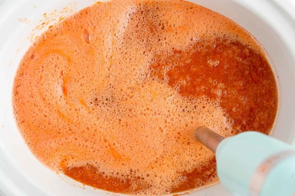 Tomato soup being blended with an immersion blender.
