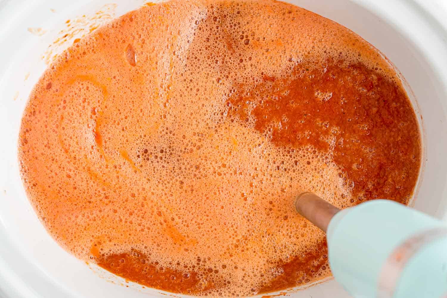 Tomato soup being blended with an immersion blender.