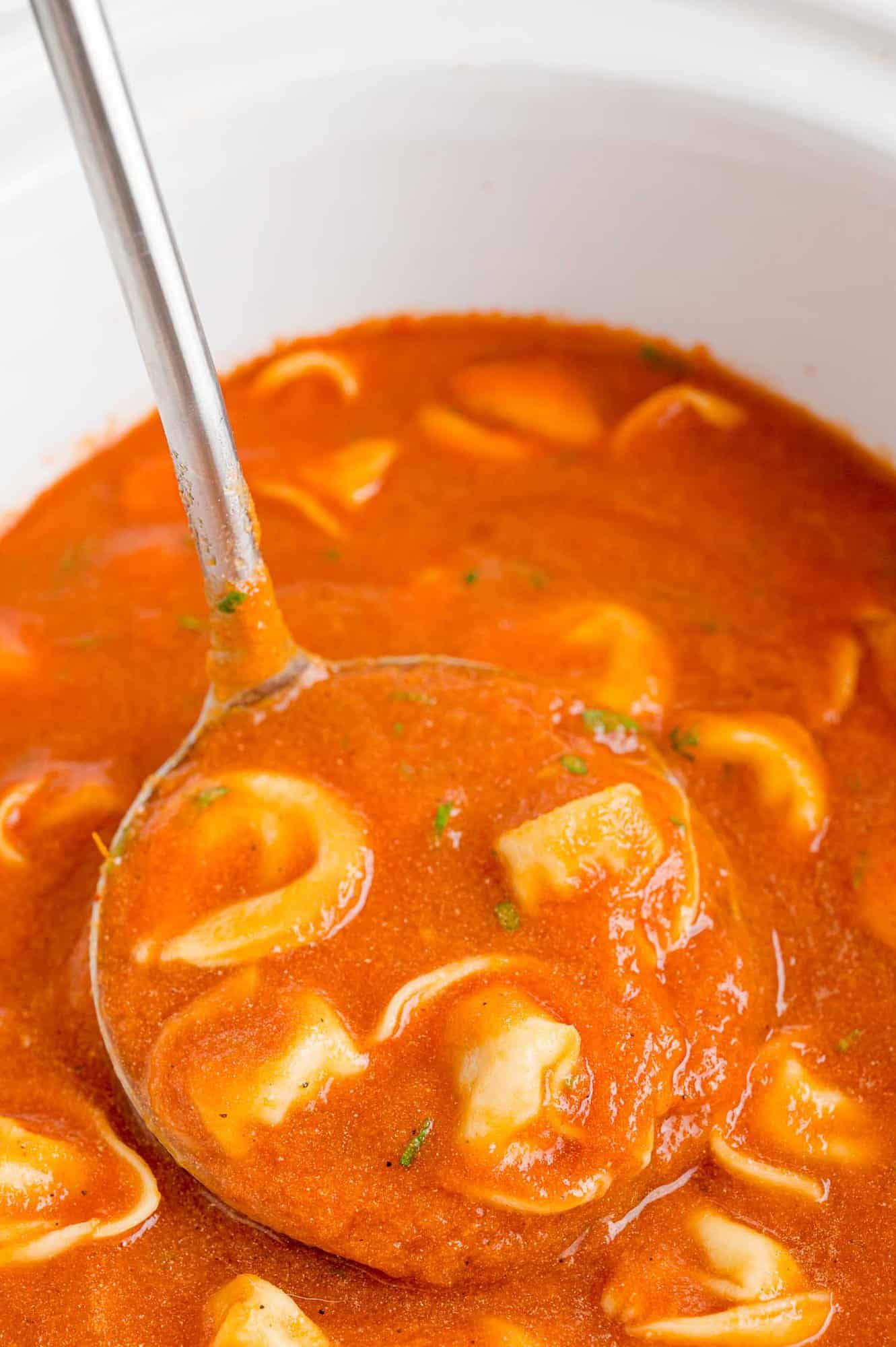 Tomato tortellini soup on a ladle, being scooped out of a slow cooker.