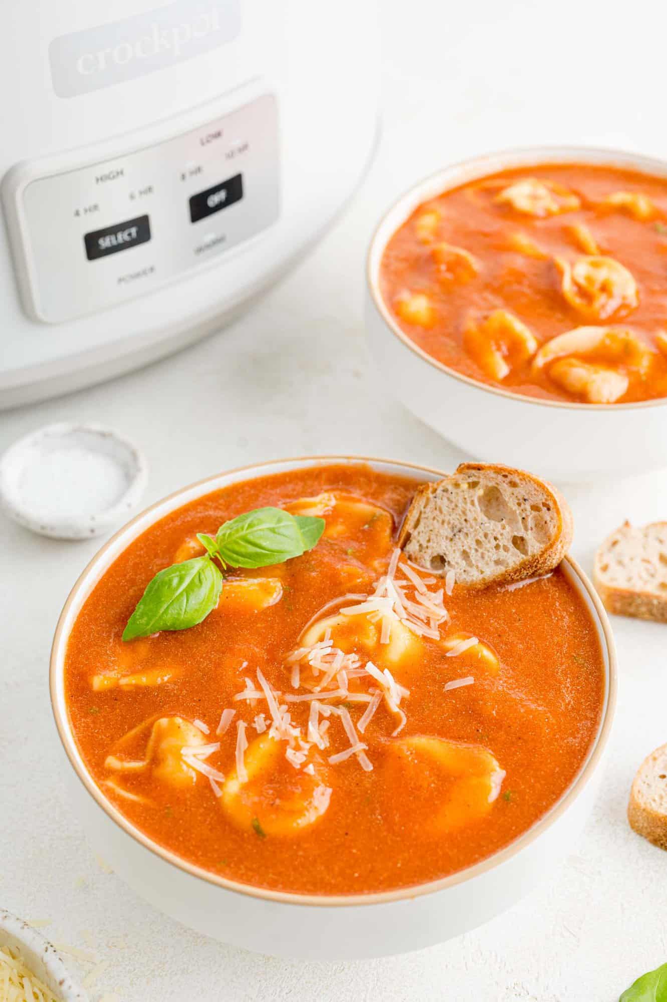 Tomato soup in white bowls with crockpot in the background.